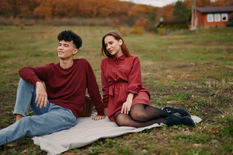 Candid portrait of a young couple sharing a relaxed countryside picnic, natural expressions and genuine connection captured in warm autumn light, conveying a truthful, lived moment.