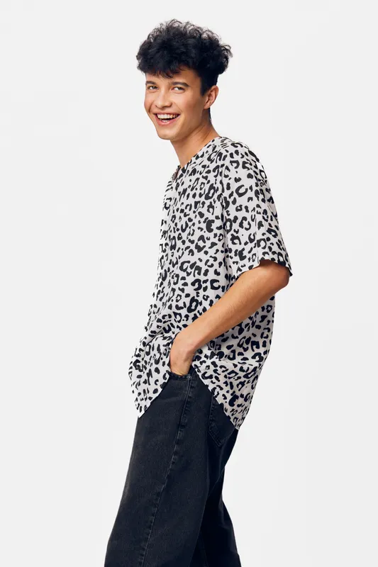 smiling man in casual leopard print shirt posing confidently with hands in pockets, short curly black hair, isolated white background, youthful style