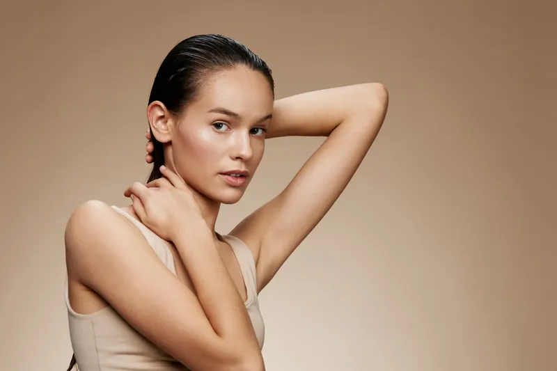 Young woman with natural beauty posing against a soft brown background, showcasing healthy skin and effortless style Perfect for beauty and skincare themes