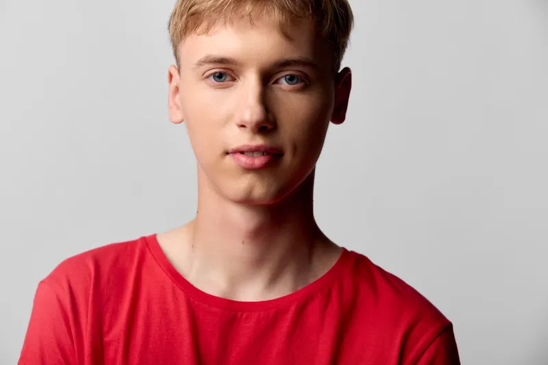 Closeup of a young man in a red shirt against a neutral studio backdrop, calm expression and soft lighting, ideal for fashion, lifestyle and stock photography projects