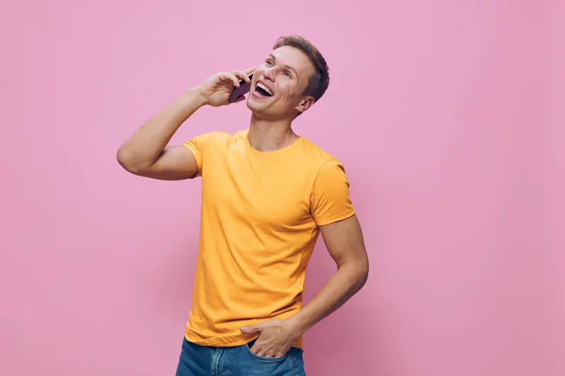 Smiling man talking on mobile phone isolated on pink background, casual clothing, cheerful mood, lifestyle concept, studio portrait, young adult male, happiness, communication, technology, relaxed atm