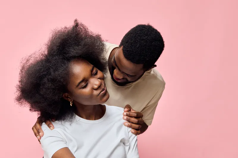 Romantic couple with expressive emotions against a pink background, showcasing love and connection through body language and soft fashion choices