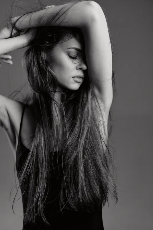 black and white portrait of a young woman with long hair posing with closed eyes in studio lighting
