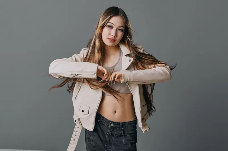 Young woman posing in casual jacket and crop top with long hair against gray background. Fashion model looking at camera with confident expression and relaxed style.