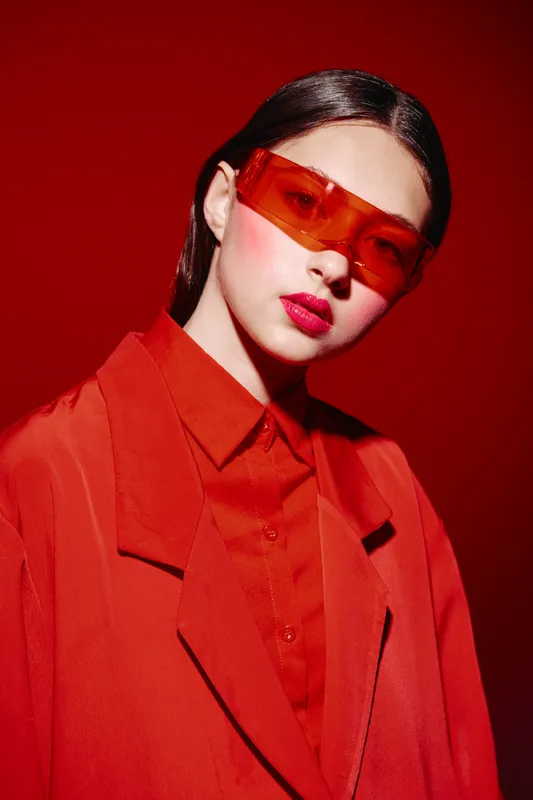 Stylish young woman with sunglasses wearing vibrant red layered clothes poses against a monotone red background full of fashion and beauty creativity ideals.