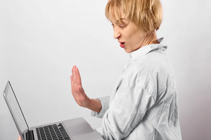 Woman at laptop, alarm and panic shouting, raised hand, computer workspace desk, close side profile view, bright white studio light, minimal background, copy space