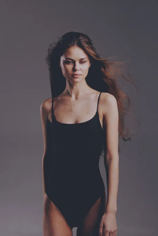 slender woman in black bodysuit with flowing hair against grey background, expressive, minimalistic, fashion portrait