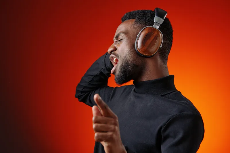 Energetic young Black man in headphones enjoying music, singing passionately against a vibrant orange background, capturing joy and creativity
