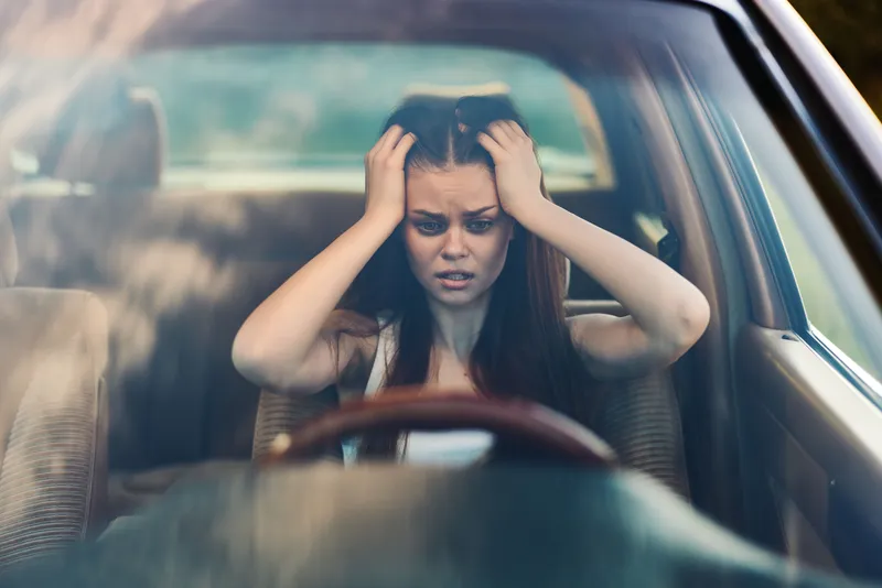 Emotional young woman feeling overwhelmed in a car, representing stress and anxiety, captured indoors with a soft focus background.