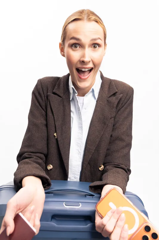 Excited young woman holding a suitcase and travel accessories against white background. Concept of travel, vacation, adventure, and tourism with happy expression and casual style.