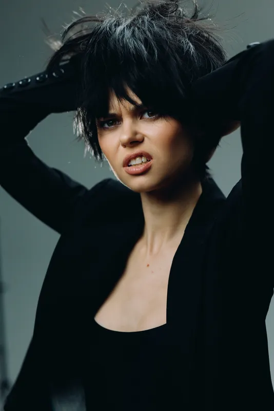 frustrated woman with messy black hair wearing black clothing expressing tension in studio setting