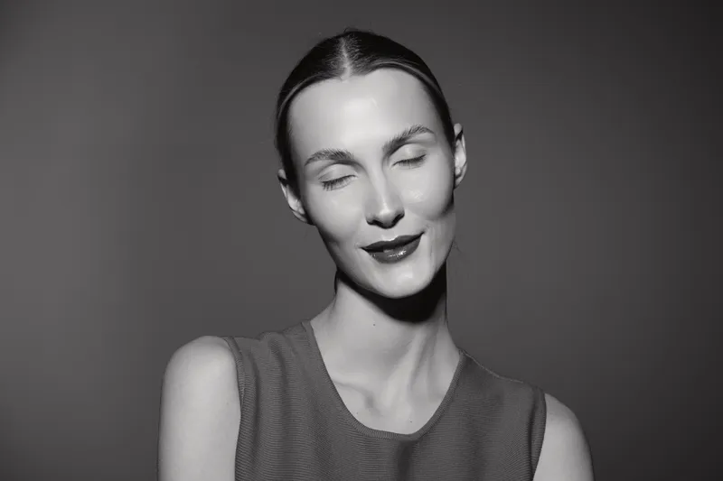 Portrait of a fair skinned Caucasian woman with closed eyes and slight smile against grey background, expressing calm and peaceful mood in monochrome.