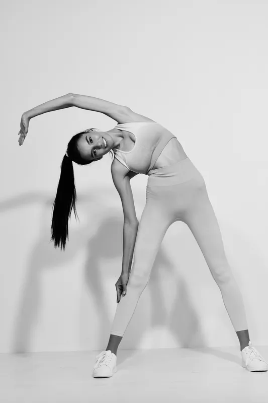 Asian woman sport fitness stretching in activewear indoors, demonstrating flexibility and balance against plain white background, black and white artistic photo.