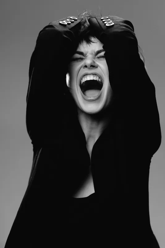Black and white portrait of shouting woman in dark clothing expressing intense emotion and frustration
