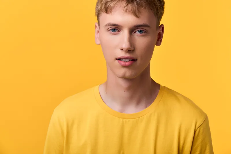 Close up of a young man in a bright yellow shirt against a vivid yellow background, showcasing casual fashion, clean lighting and modern style