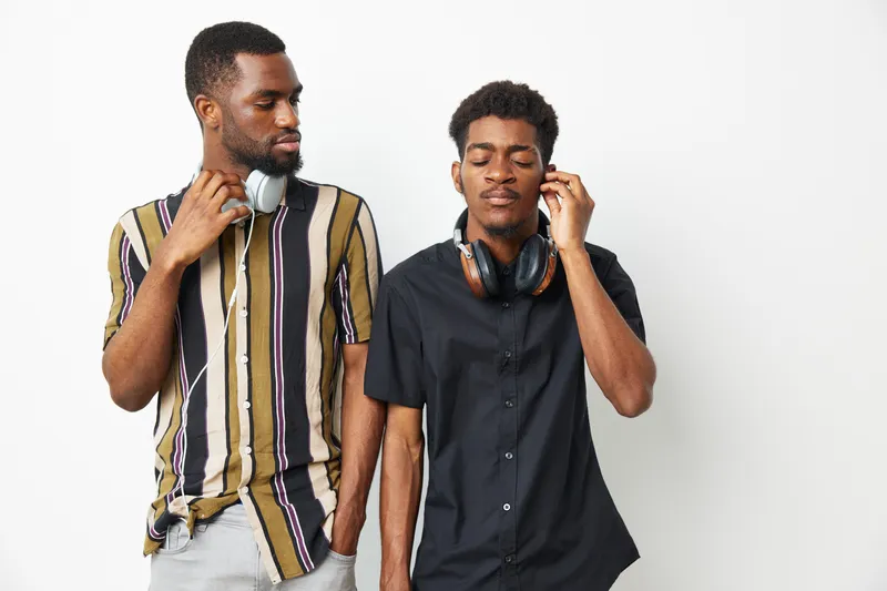 Two stylish African American men wearing headphones enjoy music together, showcasing a mood of relaxation and connection through sound and rhythm.