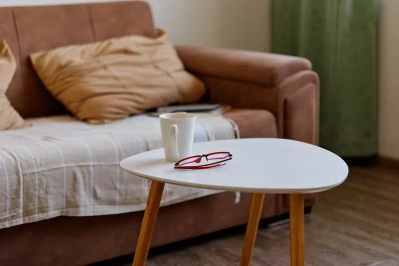 Cozy living room scene features a round white coffee table with a mug and red glasses beside a beige sofa, conveying calm home relaxation