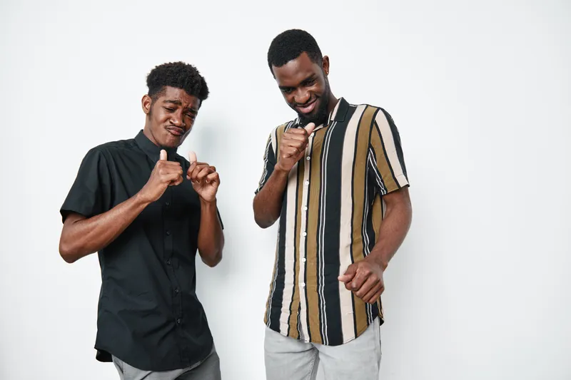 Two African American men with dark skin dancing and enjoying music together in casual clothes against white background. Friends having fun and expressing happiness indoors.