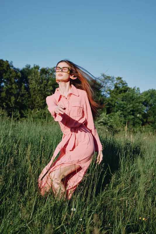Young woman in a pink dress running joyfully through a green field, showcasing freedom and vitality on a sunny day, reflecting nature s beauty and vibrant emotions
