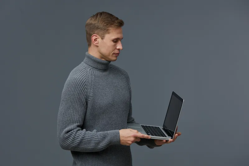 young caucasian man working with laptop using AI chat technology casual sweater isolated gray background modern digital communication concept