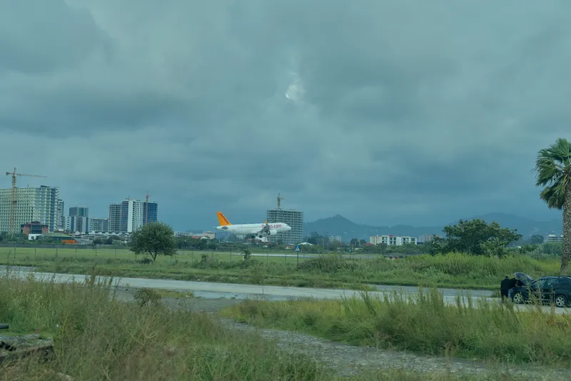 Airplane on a runway amid grassy field and distant cityscape under cloudy skies, illustrating aviation operations, takeoff preparation, and travel infrastructure