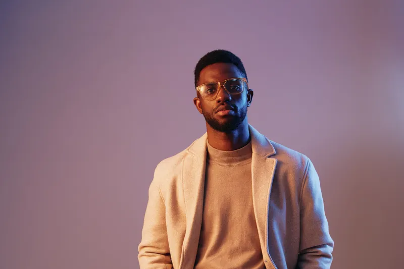 Stylish African American man in a beige coat, conveying confidence and sophistication against a soft purple background Modern fashion and emotions captured perfectly