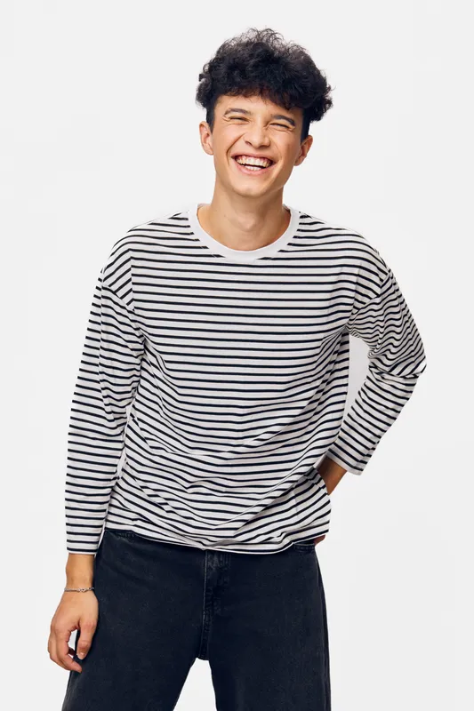 smiling man wearing striped long sleeve shirt and black jeans, casual style, joyful expression, isolated white background, young adult male