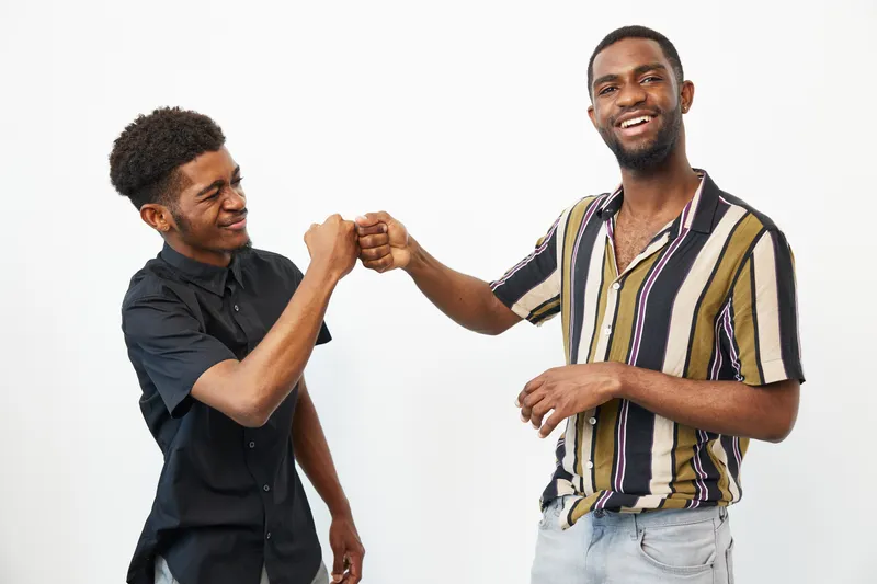 Black men sharing a joyful moment with a fist bump, showcasing friendship and camaraderie in a bright, cheerful atmosphere.