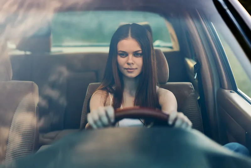 Young woman driving a car with confidence, showcasing stylish attire and a serene expression, perfect for concepts of independence and travel in vivid color.
