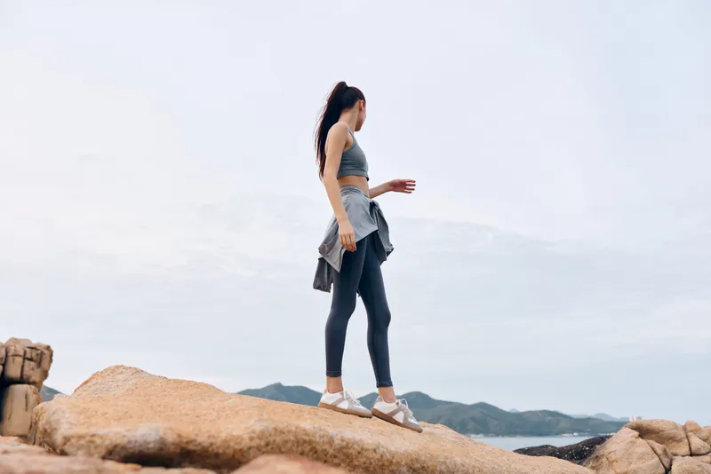 Young athletic woman in stylish sportswear walking on rocky beach, embodying a healthy lifestyle and outdoor fitness