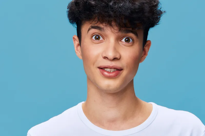 young man with curly hair wearing white t-shirt looking surprised against blue background, casual style, natural expression, studio portrait