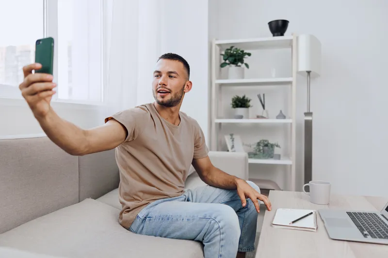 Happy man taking a selfie in a cozy, modern living room, surrounded by stylish decor and natural light, perfect for social media sharing and lifestyle content.