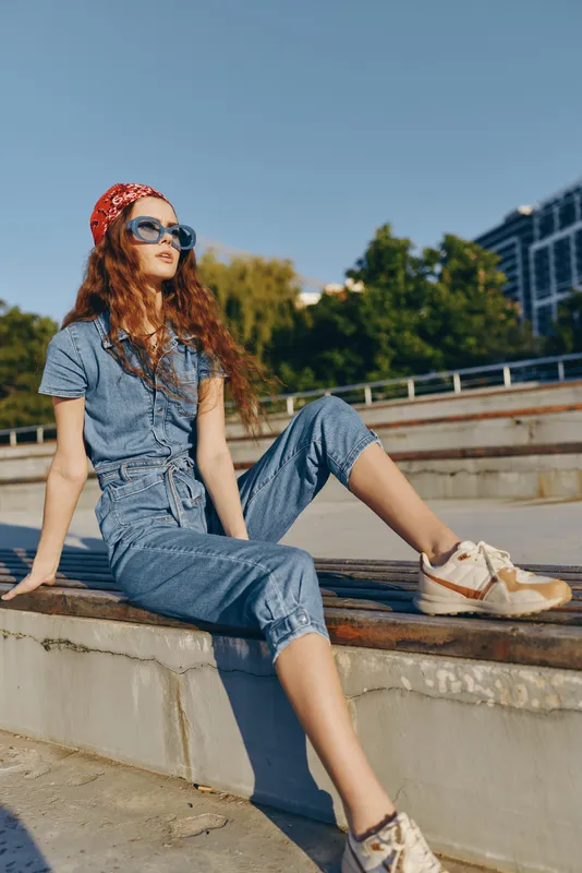 Lifestyle woman in modern boho-western denim street style relaxing outdoors with sunglasses and bandana under clear blue sky in warm natural sunlight, film color effect.
