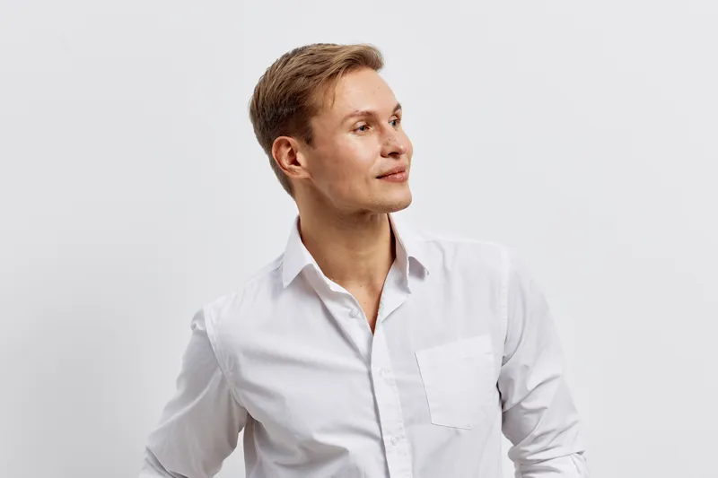 Confident young caucasian man in white dress shirt looking to the side on plain background studio portrait. People lifestyle concept