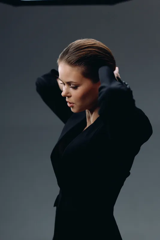 Thoughtful woman adjusting hair wearing black blazer against dark background