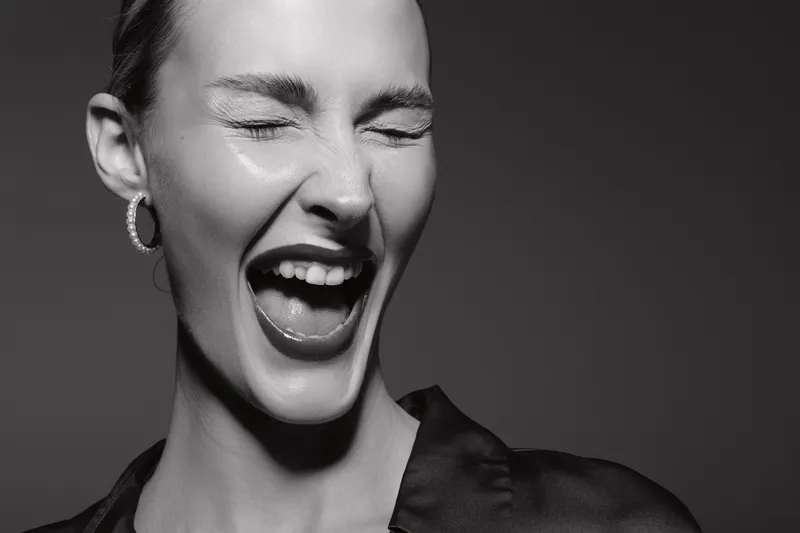 Close-up of a young white woman with fair skin laughing with eyes closed in black and white studio portrait. Concept of joy, emotion, and natural beauty.
