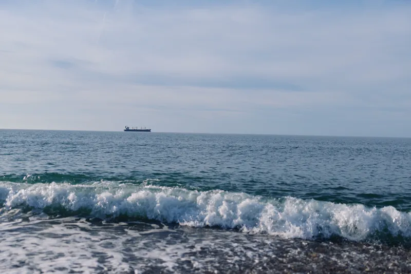 Ocean scene with calm sea, gentle waves along the shore, and a distant ship on the horizon, creating a tranquil maritime landscape suitable for travel, nature, and photography projects.
