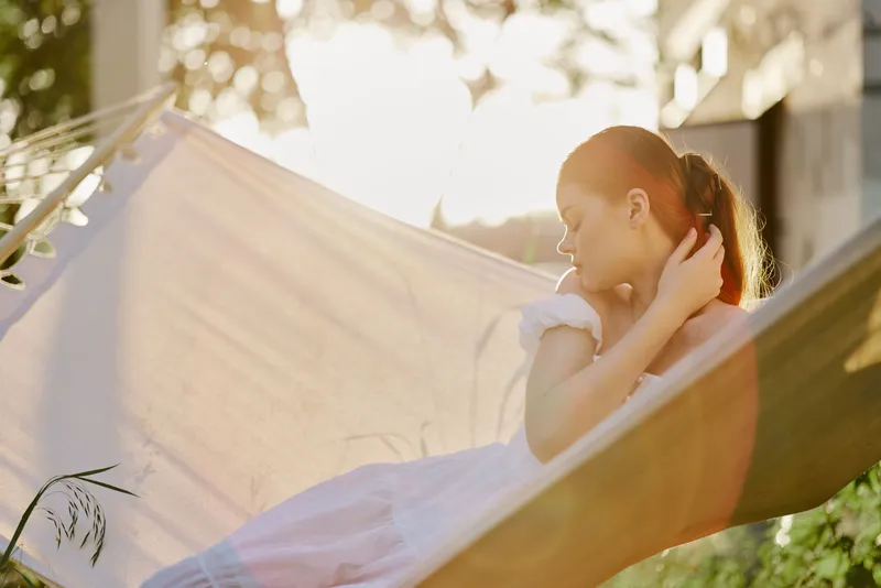 Young woman in a white dress relaxing in a hammock during sunset, embodying tranquility and peace in a serene outdoor setting