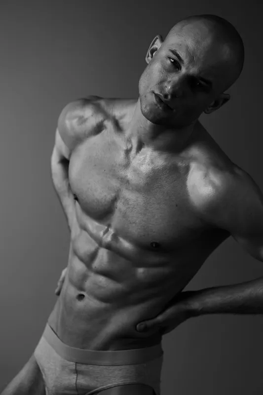 Black and white portrait of a muscular man showcasing confidence, strength, and determination, highlighting his well-defined abs and striking features.