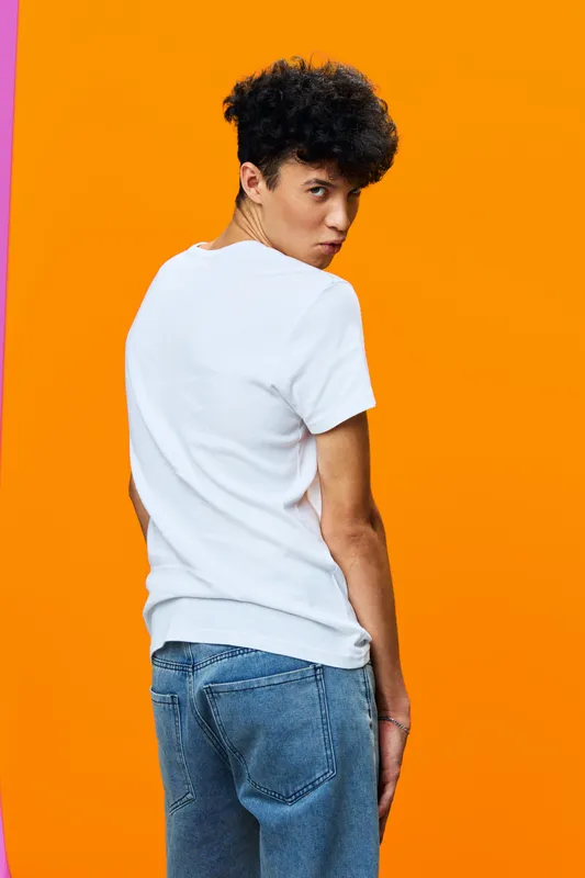 young man in white t-shirt and blue jeans posing with serious expression against bright orange background, casual style, modern fashion