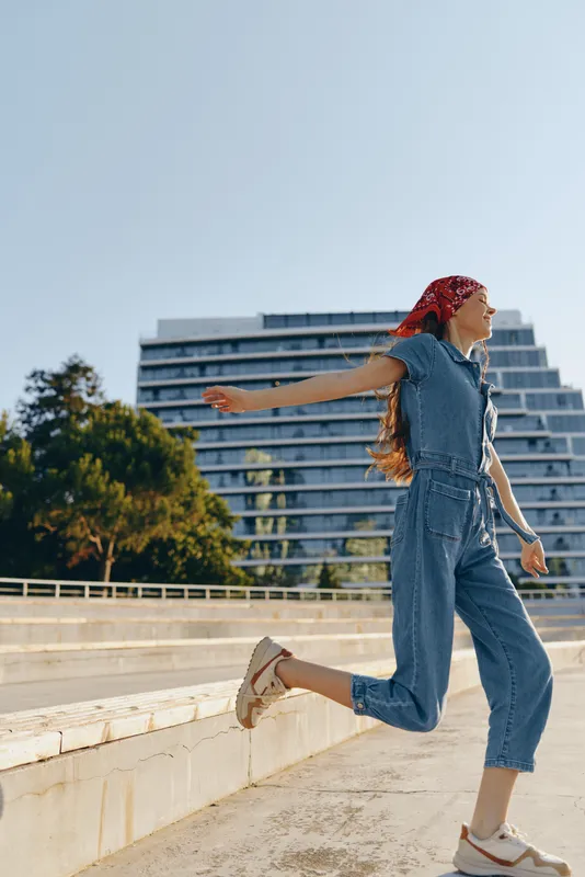lifestyle woman in modern boho-western denim street style wearing red headscarf and casual sneakers, captured with warm film color tones in urban setting