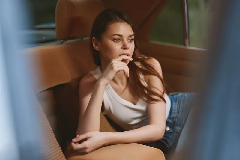 Young woman in casual wear reflecting in a vintage car interior, showcasing emotional depth and natural beauty with a warm color palette.