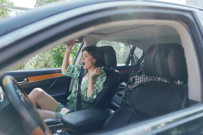 Young woman sits in a car seat, excited and expressive, raising a fist in celebration. Bright interior, casual style, and confident mood.