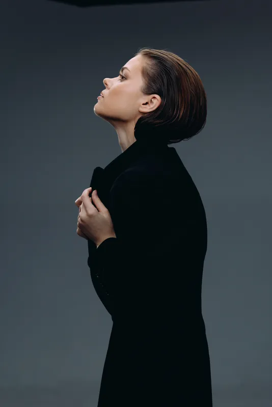 Profile of a thoughtful woman in black coat with short hair against dark background