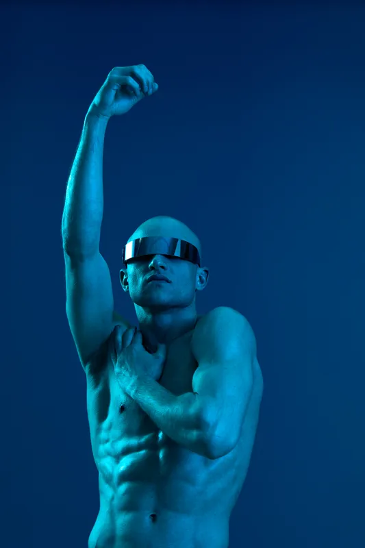 Muscular man in stylish sunglasses showcases confidence against a blue backdrop, emphasizing strength and modernity in this eye-catching image.