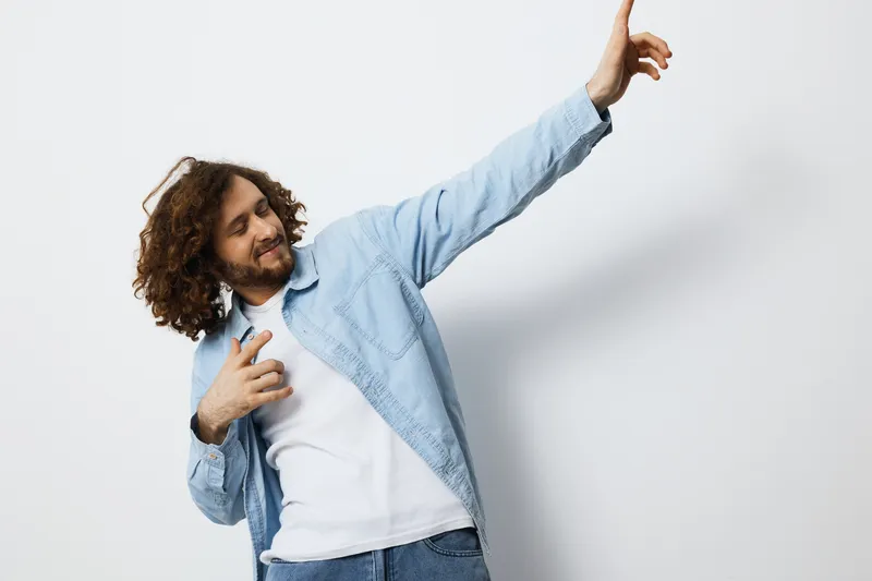 Young man dancing joyfully in a casual denim shirt against a light background, showcasing a vibrant and energetic mood