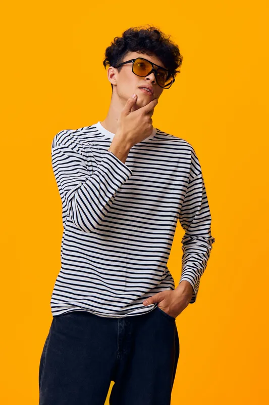 young man with curly hair wearing striped shirt and sunglasses posing confidently against a bright orange background in casual style