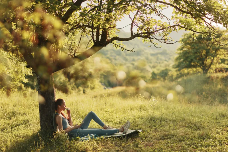 Young woman enjoying a peaceful moment under a tree in a green meadow, wearing casual clothing, reflecting tranquility and nature s beauty