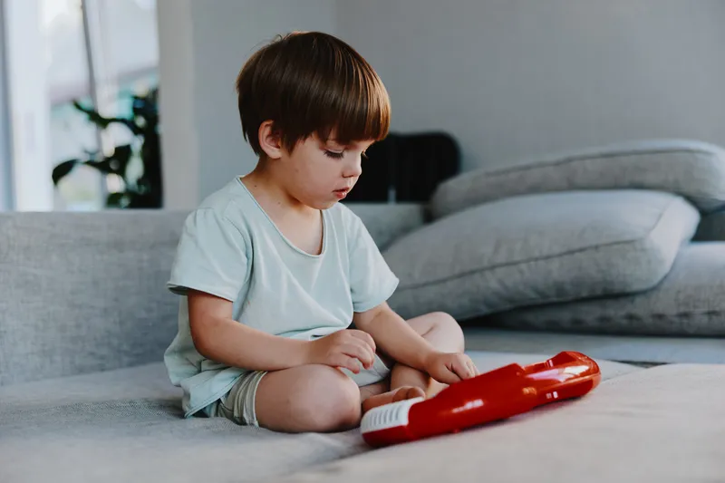 Focused boy playing a toy keyboard, showcasing creativity and joy in a cozy living room environment. The soft lighting enhances a playful atmosphere.