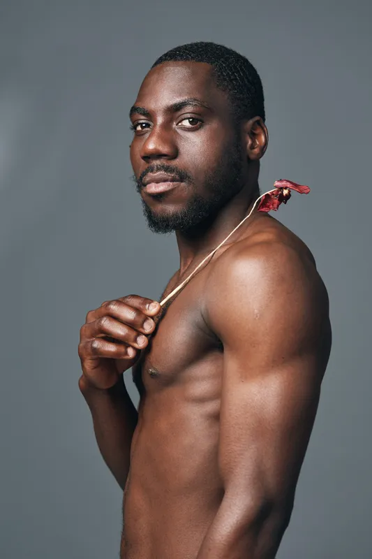 African man with dark skin and muscular body posing shirtless with creative conceptual style on gray background. Portrait of confident male model with artistic visual expression.